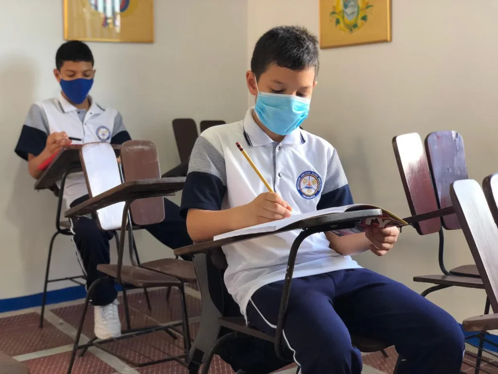 Estudiante con polo institucional escribiendo en su pupitre