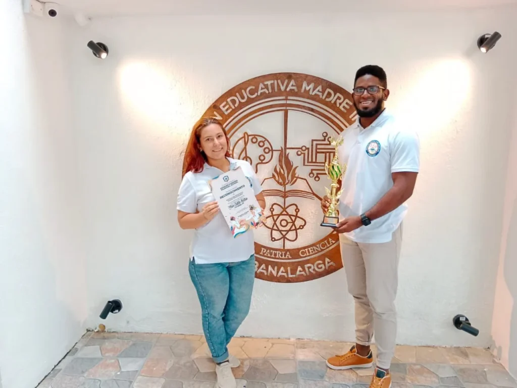 Dos exalumnos con un diploma y un trofeo frente al escudo de la Institución Educativa Madre Inmaculada