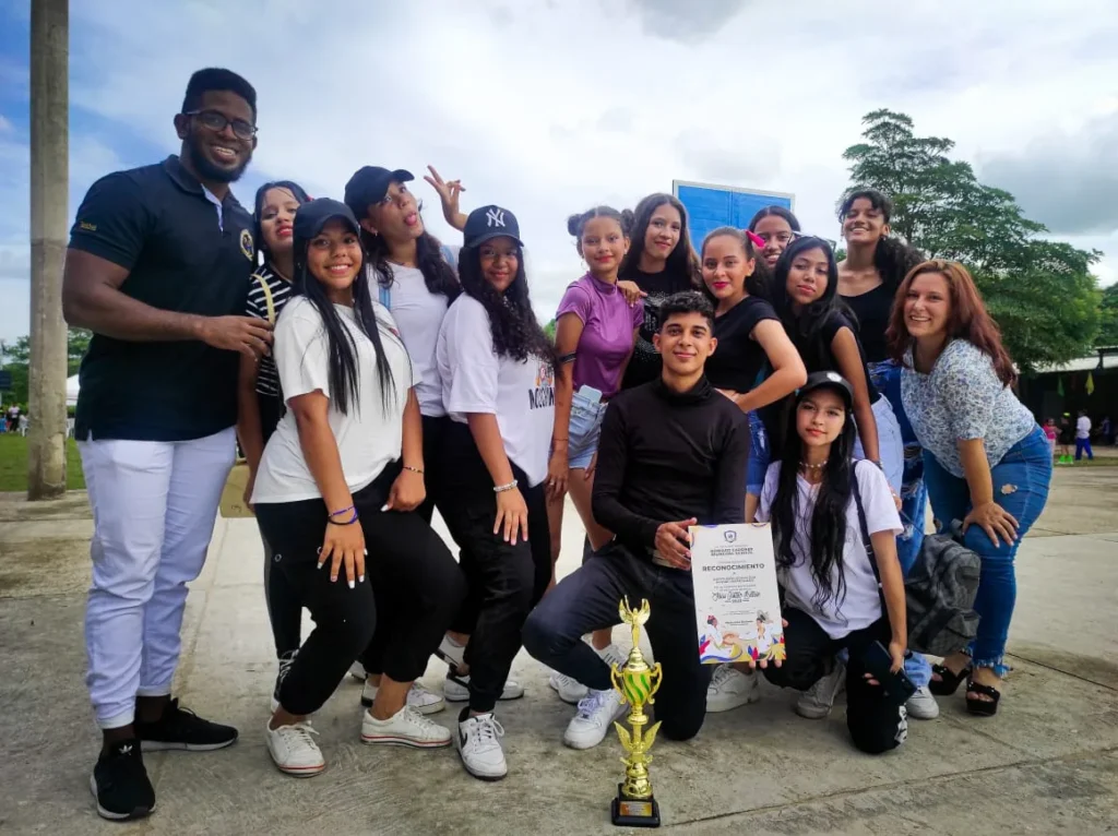 Grupo de exalumnos posando al aire libre con un trofeo y un diploma