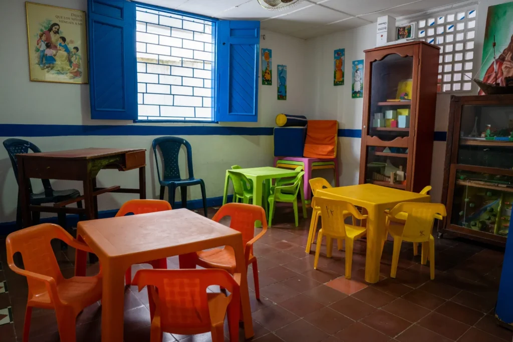 Rincón de juego de preescolar con mesas amarillas, sillas de colores y estantes