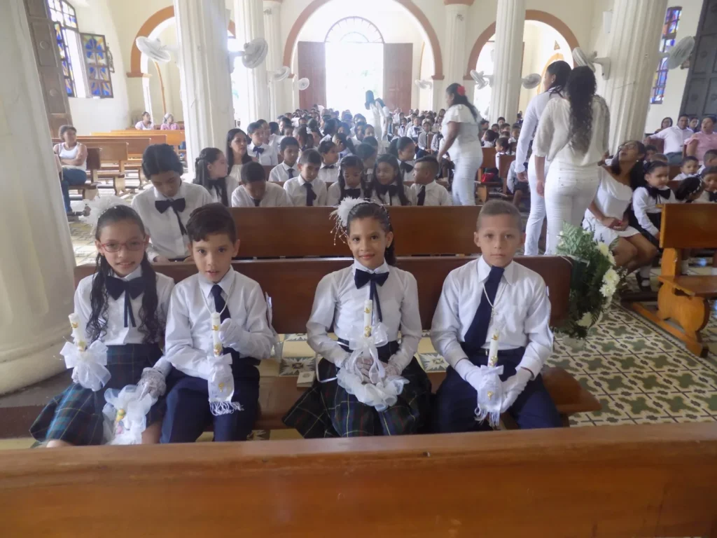 Niños con camisa blanca y corbatín sentados en la iglesia durante una celebración religiosa