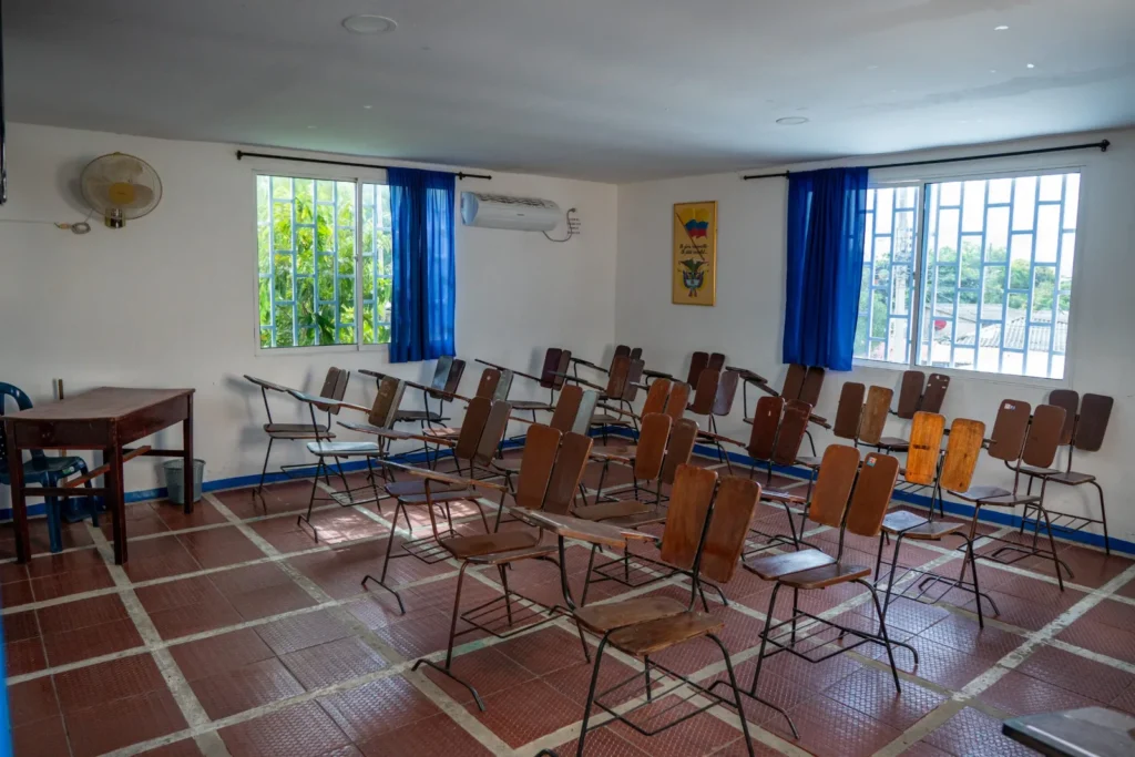 Salón de clases luminoso con ventanas, pupitres y ventilador